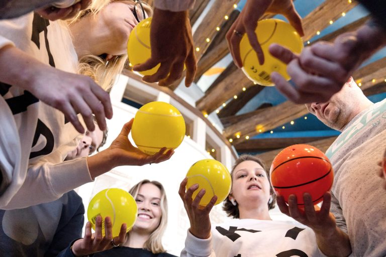 Kind artikkelikuva ryhmäharjoituksesta, jossa työntekijöillä on keltaisia palloja käsissä.